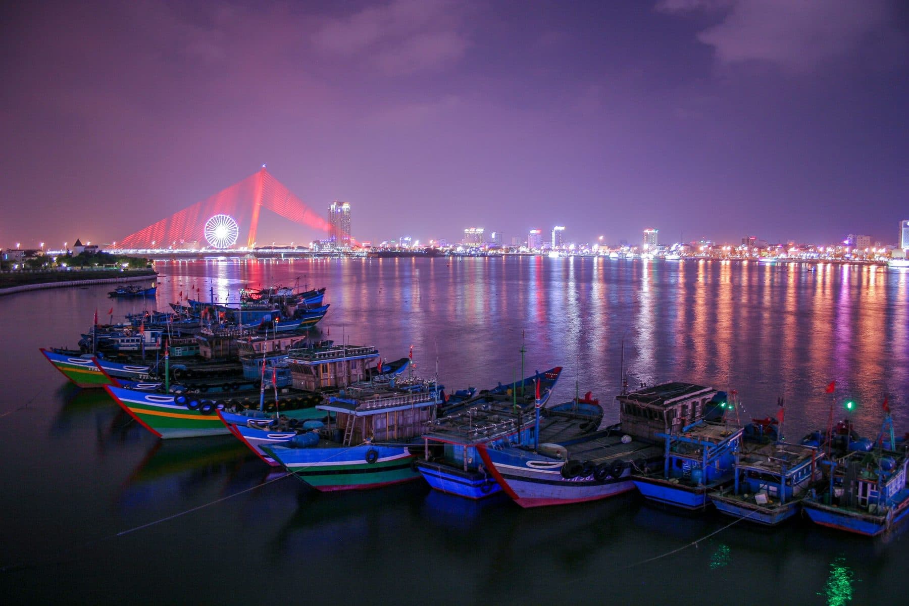 Fishing boats on the Han River at night, with the Sun Wheel and the Tran Thi Ly bridge lit behind them
