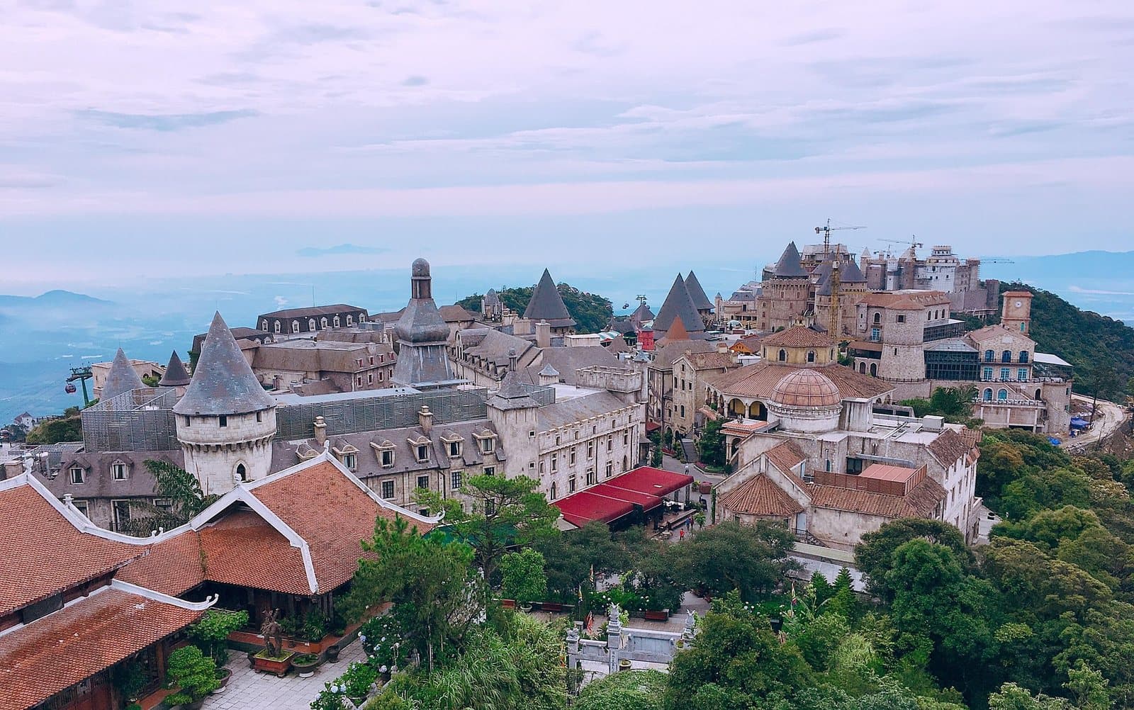 Làng Pháp tại Sun World Ba Na Hills nhìn từ trên cao: những tháp mái nhọn lợp đá, một mái vòm, mái ngói đỏ và một cabin cáp treo ở bên trái