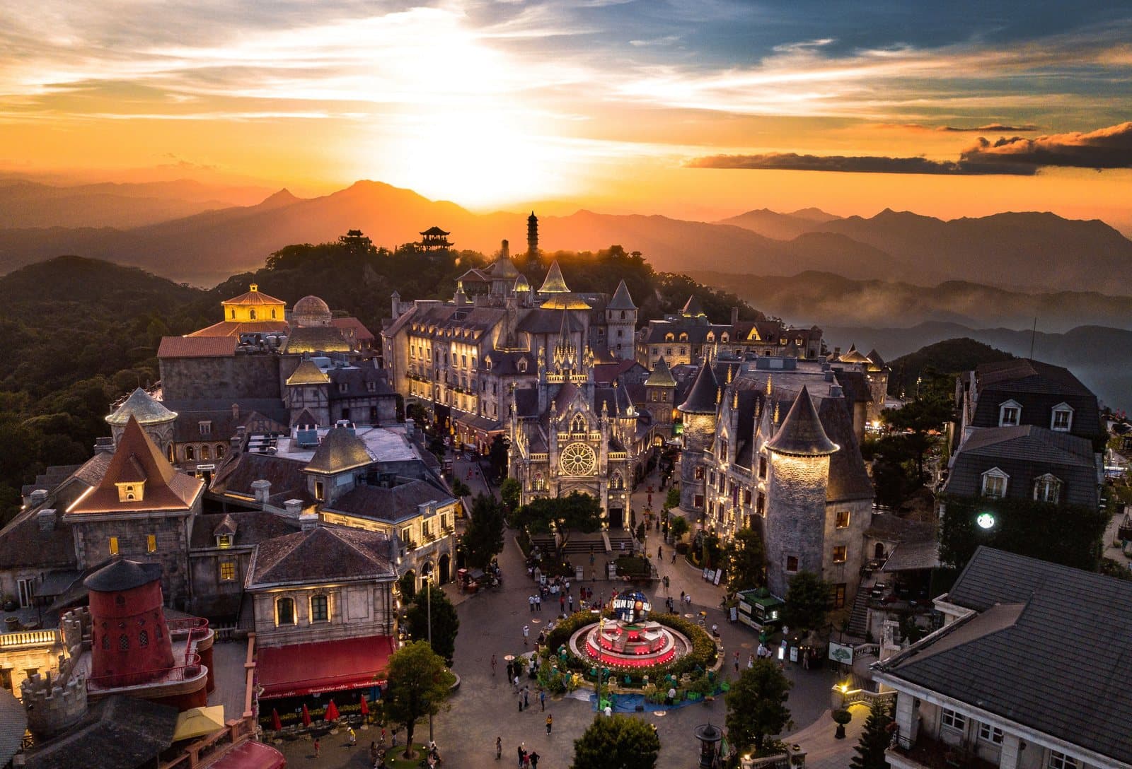 Làng Pháp tại Sun World Ba Na Hills nhìn từ trên cao lúc hoàng hôn: nhà thờ có cửa sổ hoa hồng, những tháp tròn, phố lên đèn và đài phun nước hình quả cầu giữa quảng trường