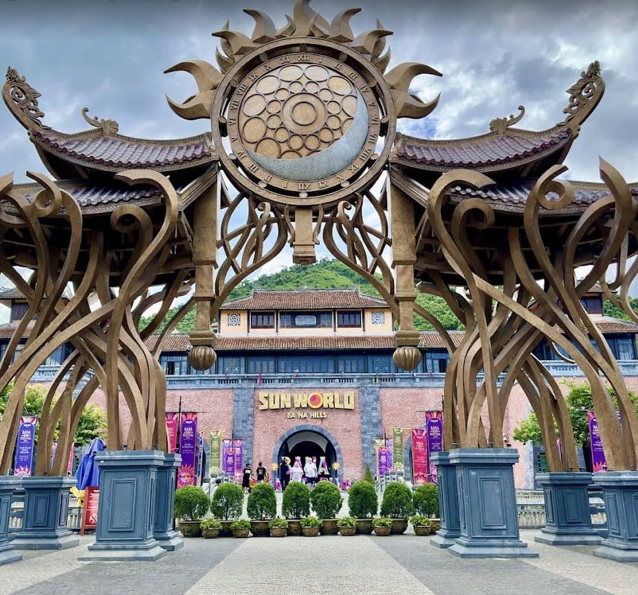 Cổng đồng uốn lượn dưới mặt đồng hồ hình mặt trời và mặt trăng, phía trước bảng tên Sun World Ba Na Hills