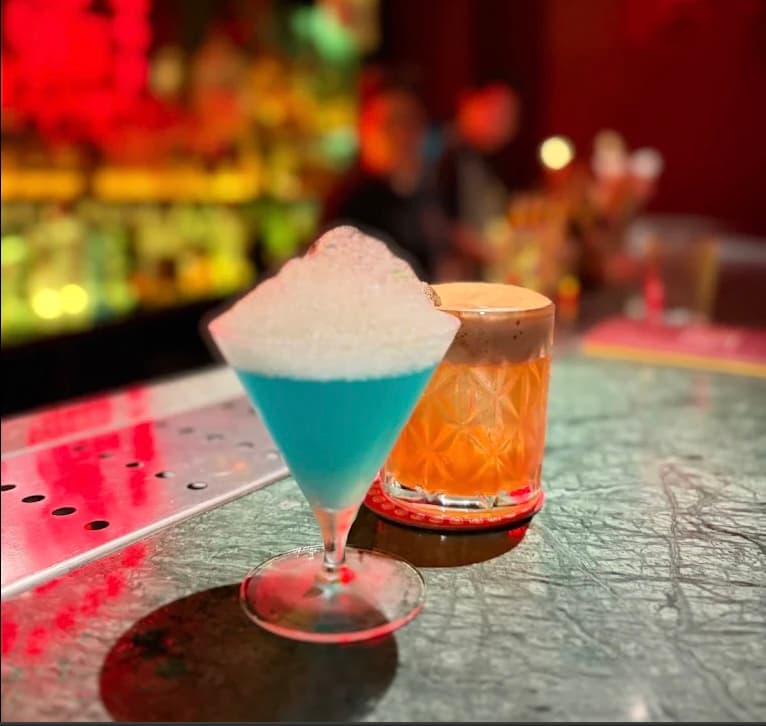 A blue cocktail and an orange cocktail on the bar at Bar Đồ Yêu