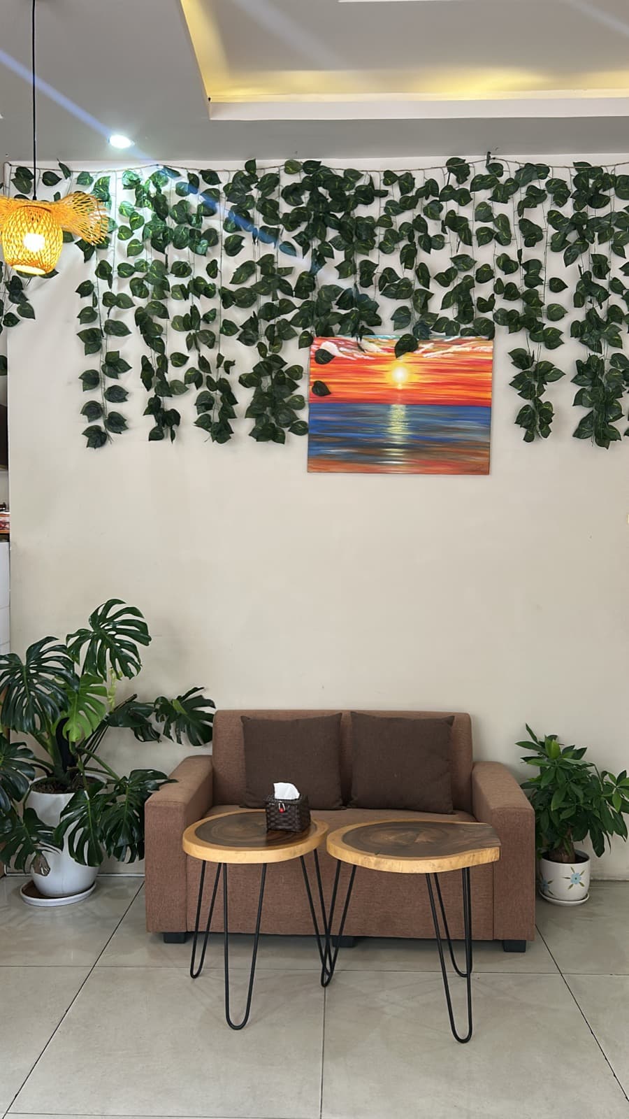 Inside Bien Cafe, a sofa under hanging ivy and a painted sunset over the sea, in Da Nang