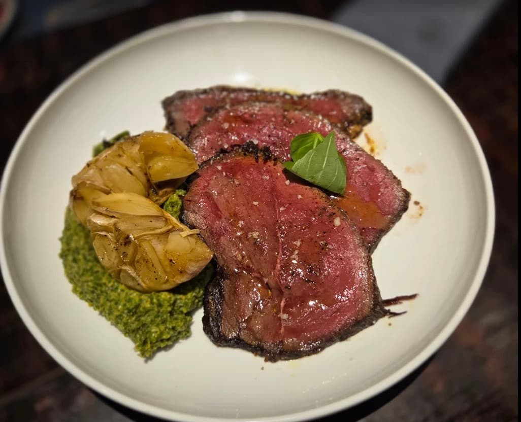 Cucina Luca, những lát thịt bò hồng nướng với một củ tỏi nướng trên sốt xanh