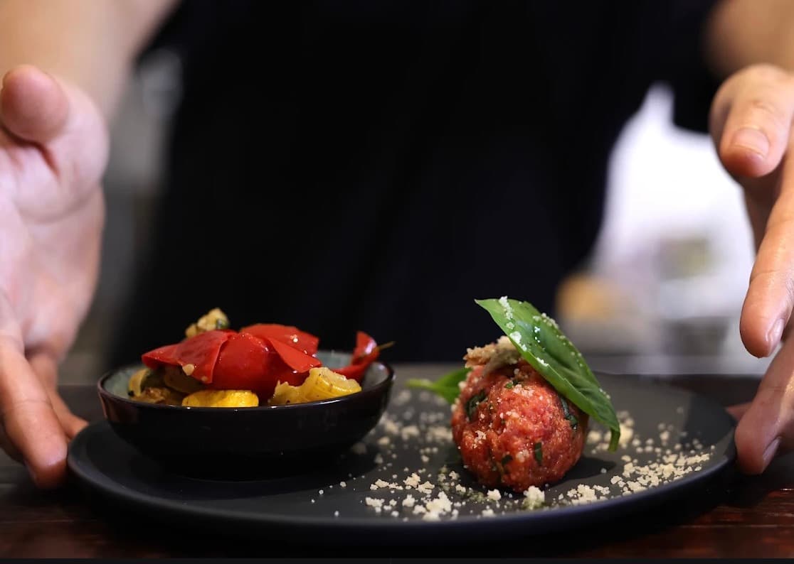 Cucina Luca, một viên thịt băm phủ lá húng quế, bên cạnh chén ớt chuông