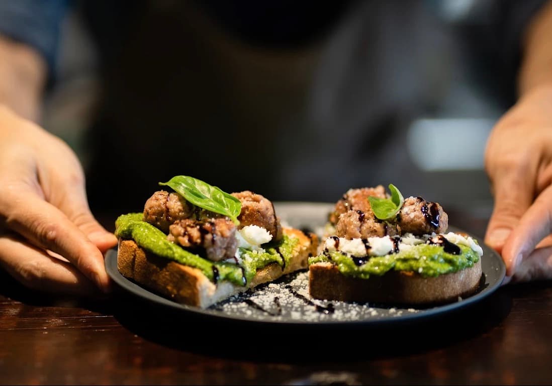 Cucina Luca, bánh mì nướng phủ sốt pesto xanh, thịt, phô mai trắng và húng quế, đặt trên hai bàn tay