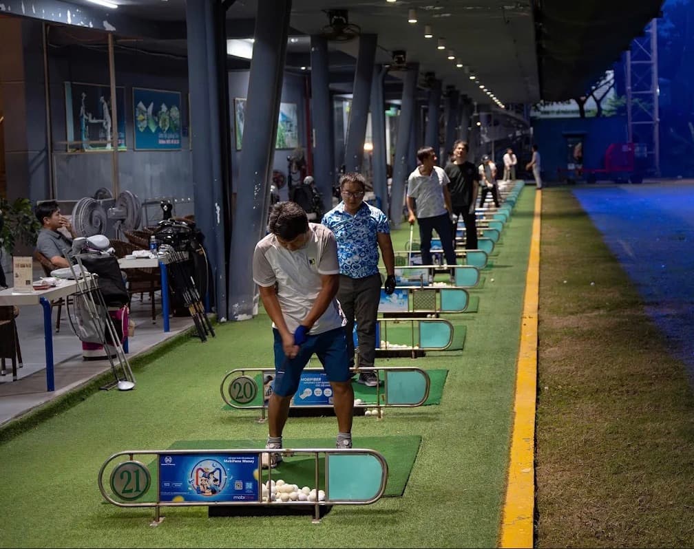 Golf DNC, a row of numbered hitting bays lit in the evening, players at the mats