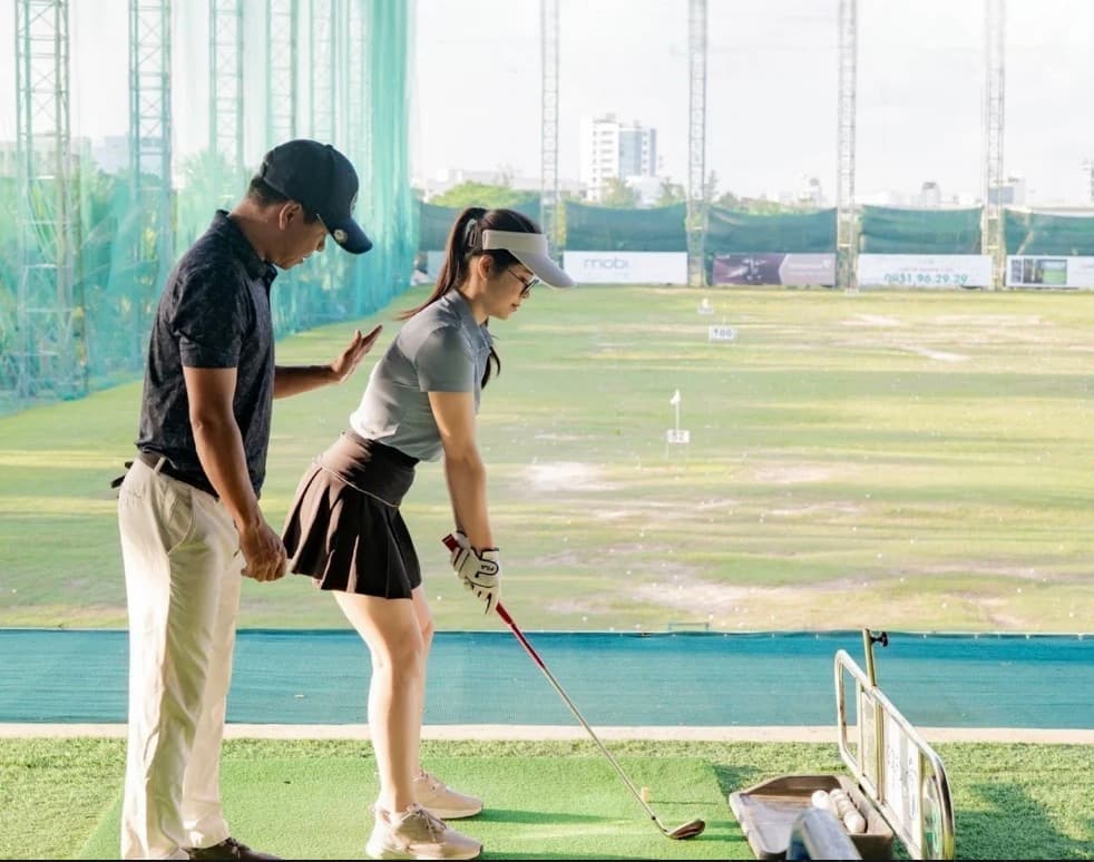Golf DNC, a man standing beside a woman as she lines up a shot at a bay