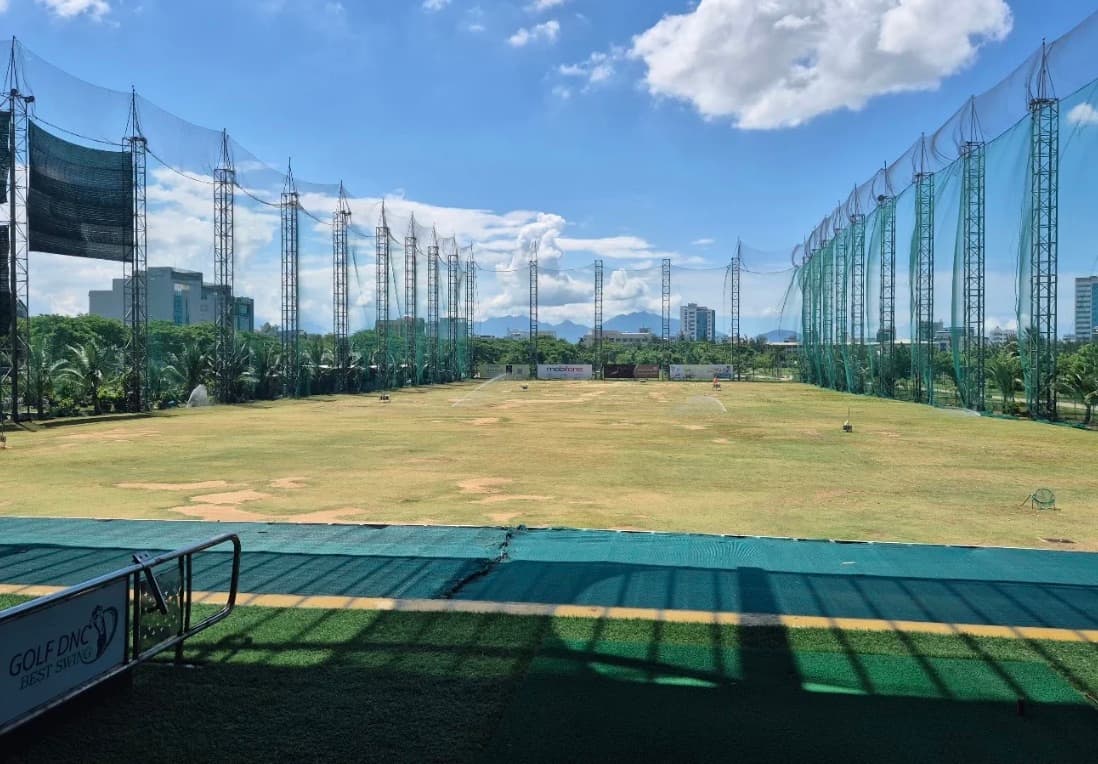 Golf DNC, the range from the bays on a clear day, a grass field with target flags between tall net towers, and the range's sign in the corner