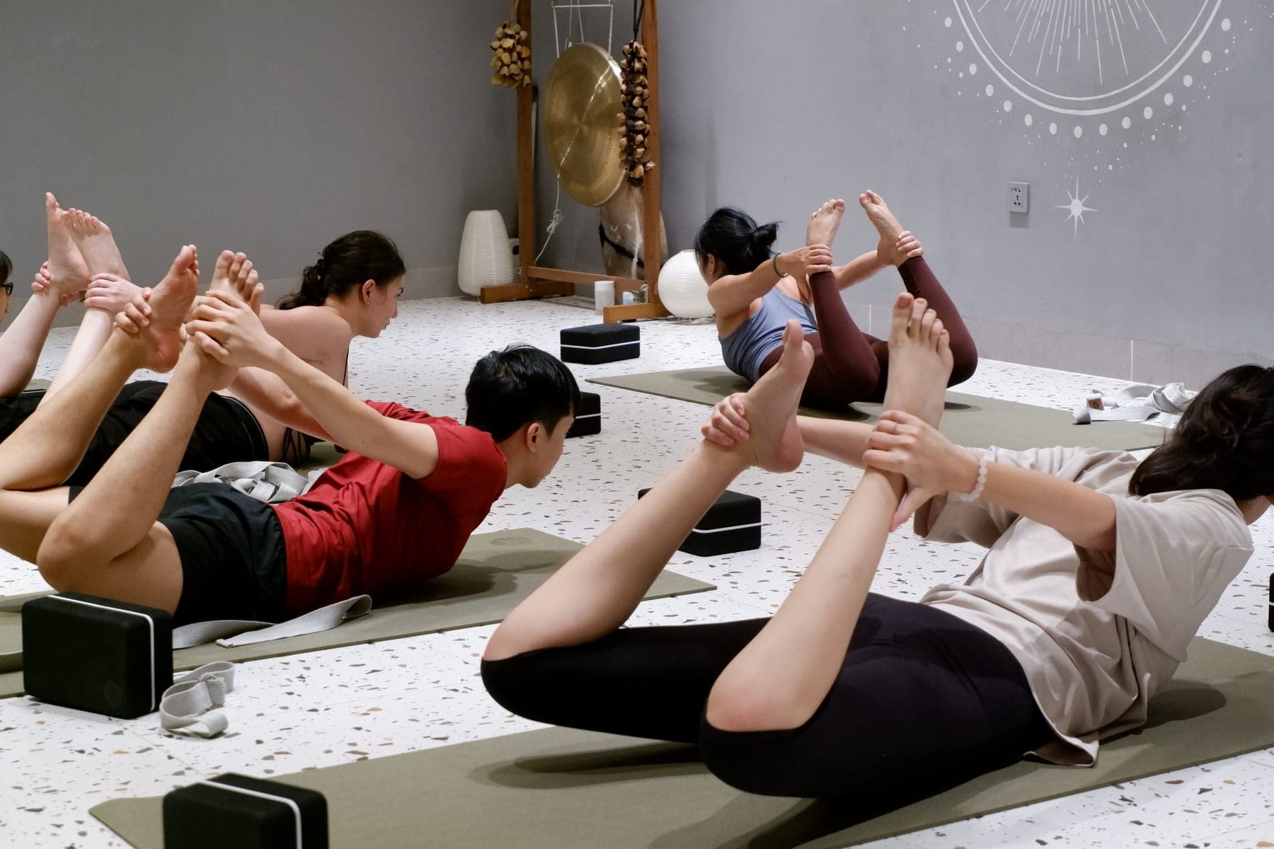 Học viên tập tư thế cánh cung trên thảm xanh ở Heart Studio by Chan, phía sau là chiếc cồng trên giá gỗ