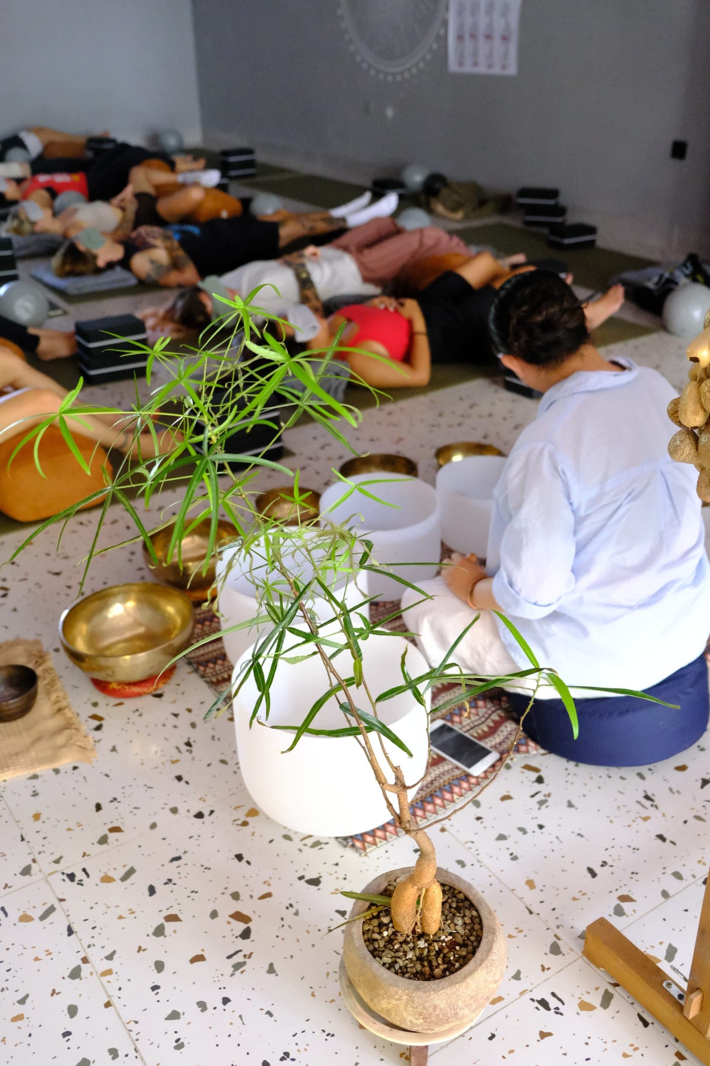 Một người ngồi giữa những chiếc chuông xoay trắng và chuông xoay đồng ở Heart Studio by Chan, phía sau là lớp đang nằm trên thảm