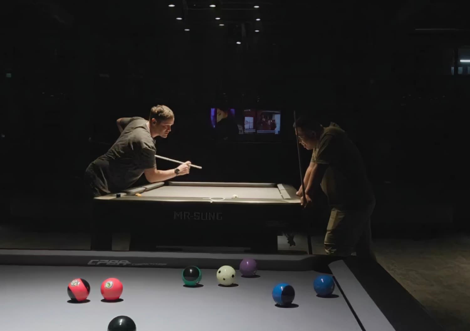 Hybrid, players at a pool table with screens behind