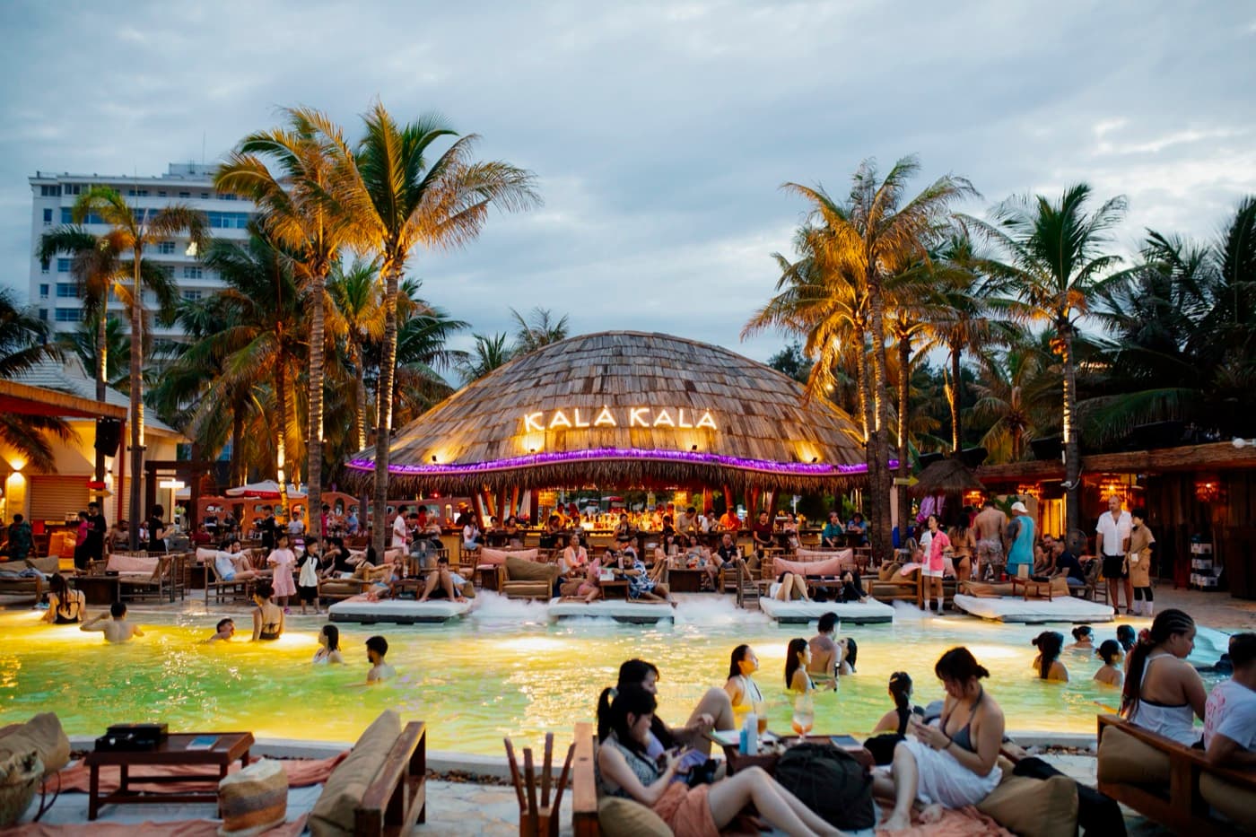 Kalà Kalà Beach Club, the round thatched bar with the Kala Kala sign at dusk, the lit pool and palm trees