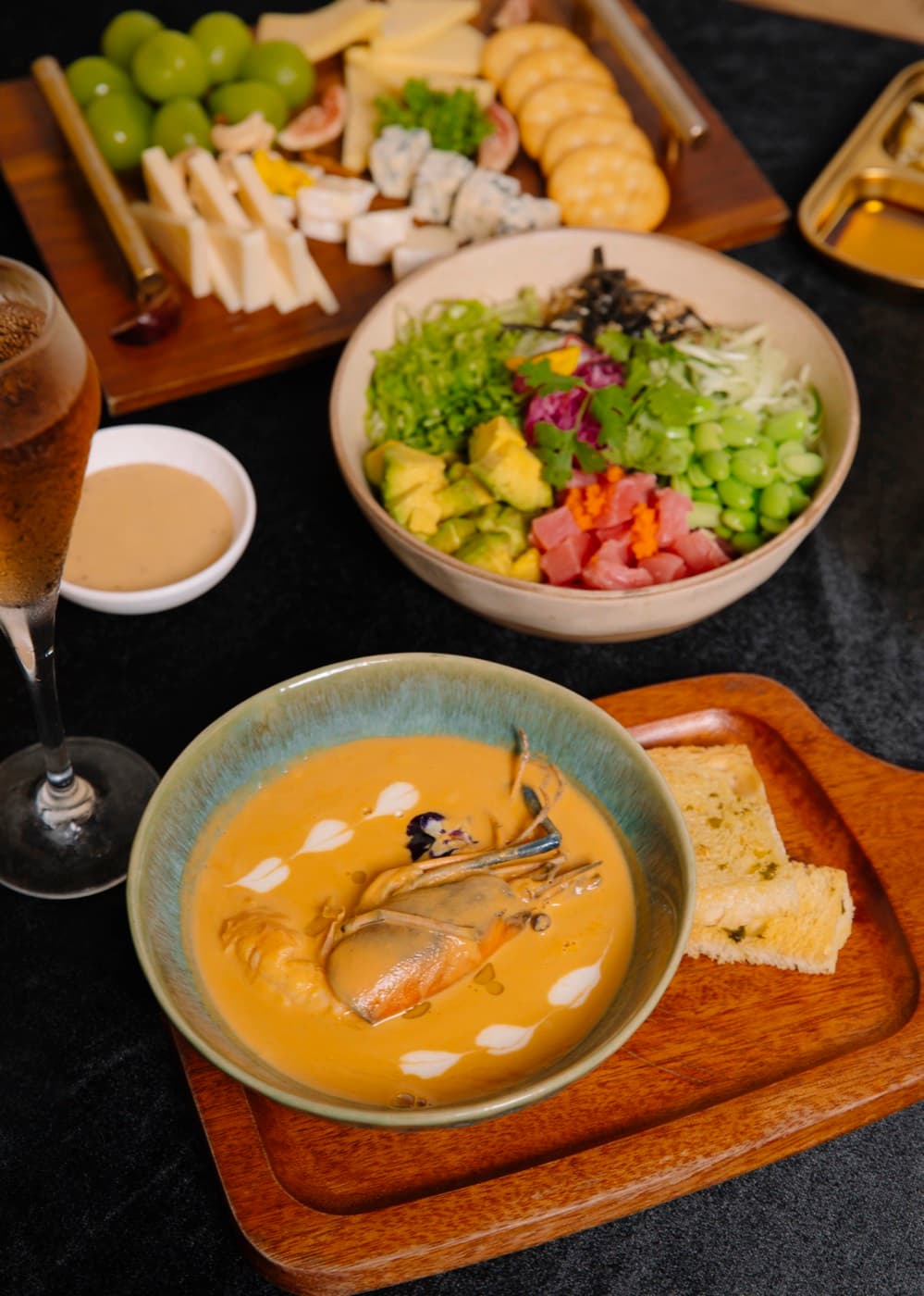 Kalà Kalà Beach Club, a bowl of soup with a prawn, a bowl of greens, avocado and diced fish, a cheese board and a glass of sparkling wine