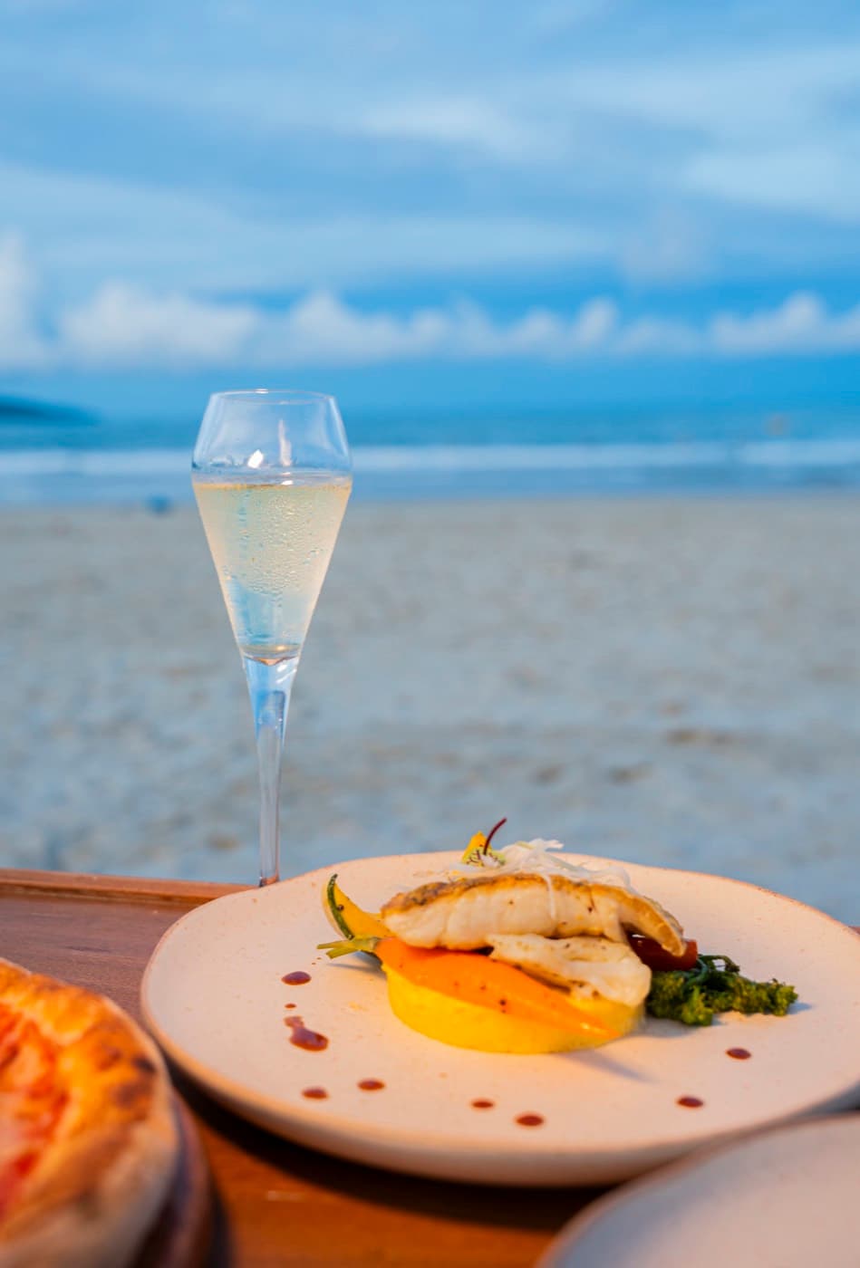 Kalà Kalà Beach Club, a fillet of fish on carrots, with a glass of sparkling wine and the beach behind
