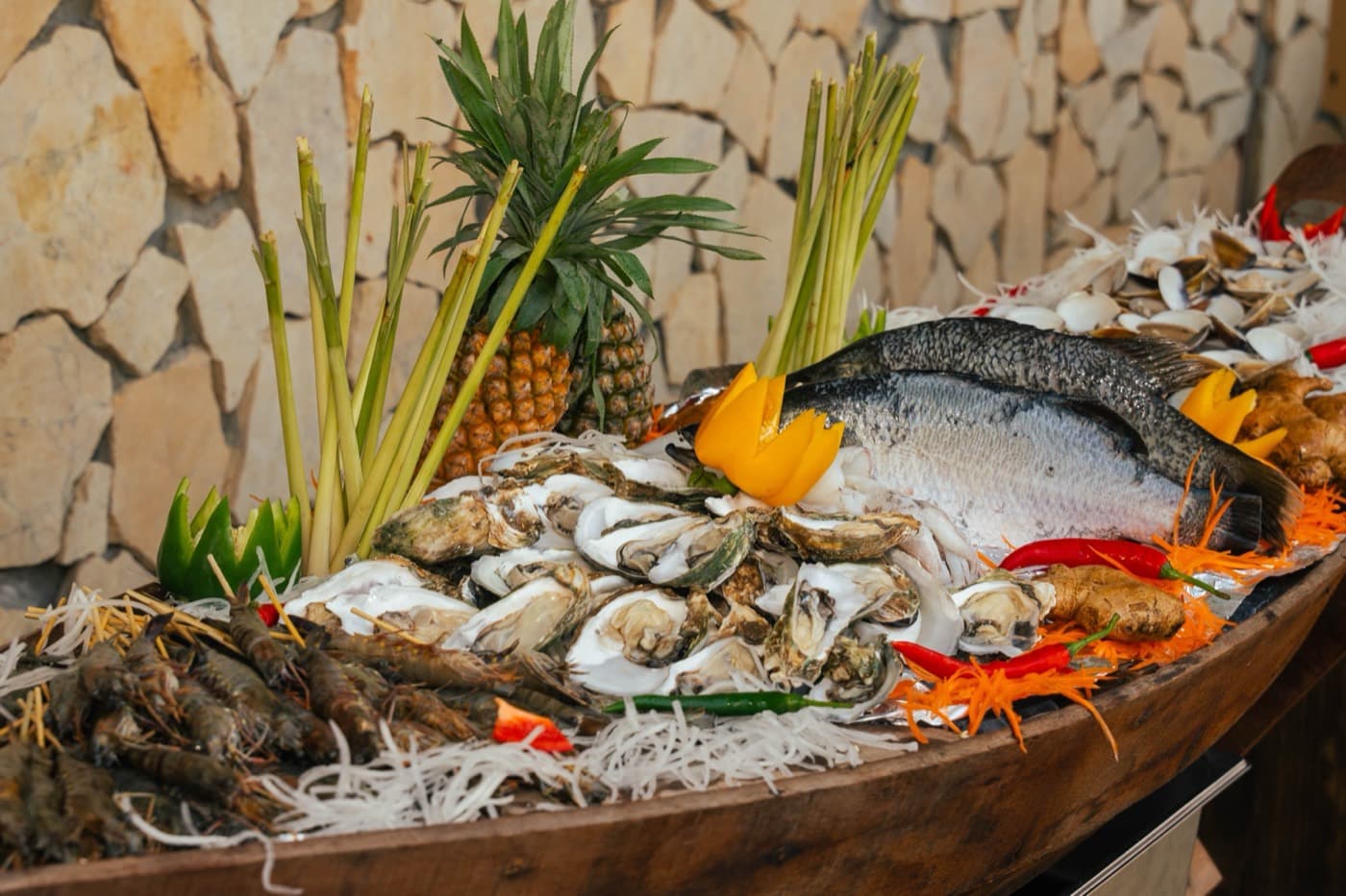Kalà Kalà Beach Club, raw seafood laid out in a wooden boat, oysters, prawns, clams and two whole fish, with pineapple and lemongrass