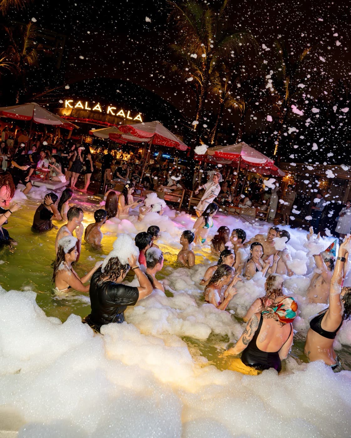Kalà Kalà Beach Club, a crowd in the pool in white foam at night, under the lit Kala Kala sign
