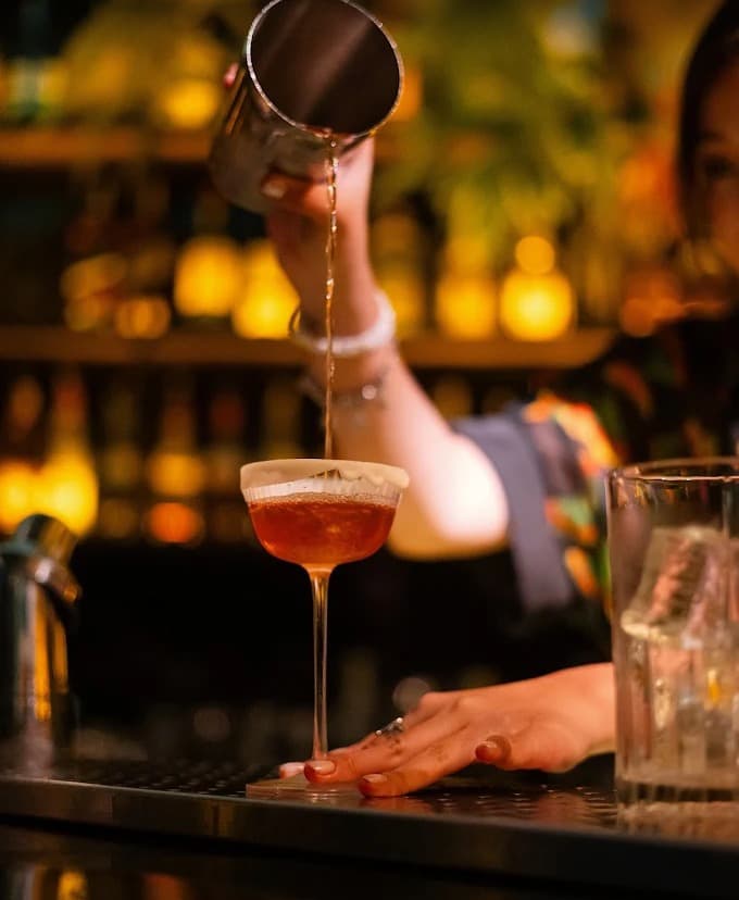 A bartender at Ket High Cocktail Bar pours a cocktail from a tin into a glass on the bar