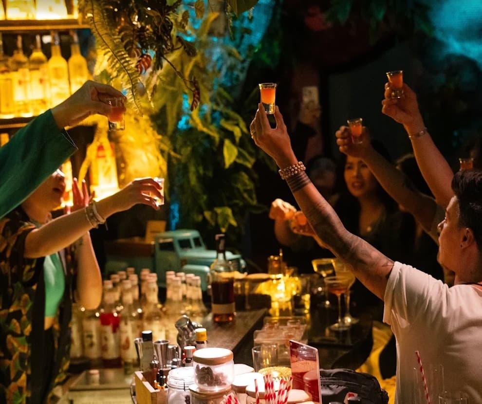 Guests and a bartender at Ket High Cocktail Bar raise small glasses over the bar