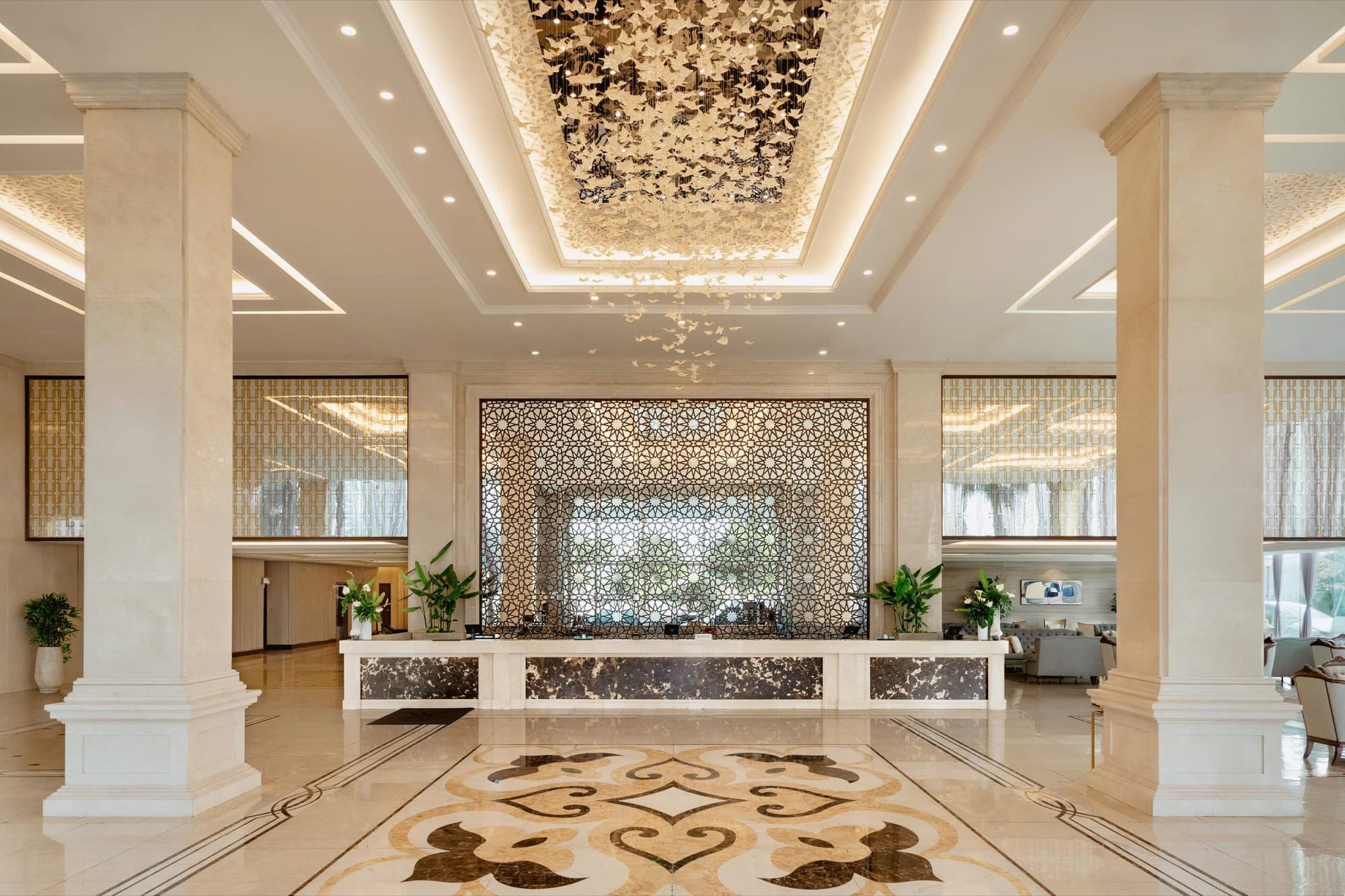 Sảnh Meliá Vinpearl Danang Riverfront: cột đá cẩm thạch, quầy lễ tân, tấm bình phong chạm hoa văn phía sau và những khối trang trí màu trắng rủ xuống từ trần