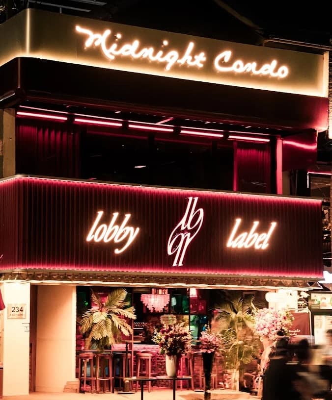 The shop front of Midnight Condo at night, with its lit sign above the street