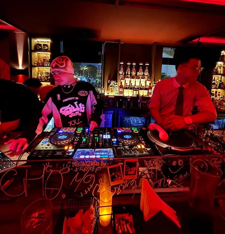 A DJ plays at the decks on the bar at Midnight Condo, beside a bartender in a tie
