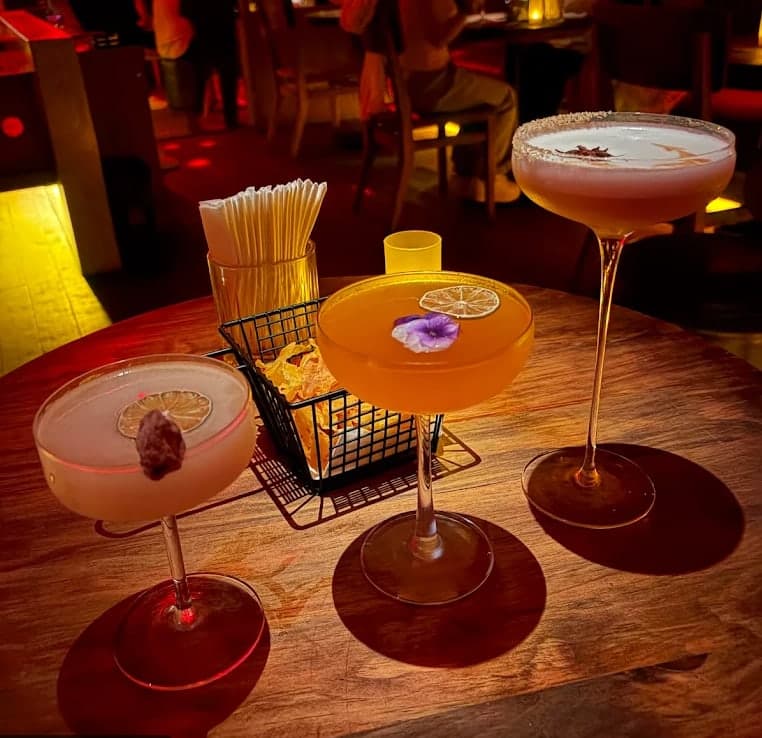 Three cocktails on a round wooden table at Midnight Condo
