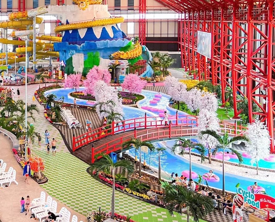 Mikazuki Water Park 365, tháp đường trượt trong nhà có ống trượt màu vàng và con rồng vàng quấn quanh tháp, cây cầu đỏ bắc qua dòng sông có phao hồng, cùng những cây hoa màu hồng và trắng