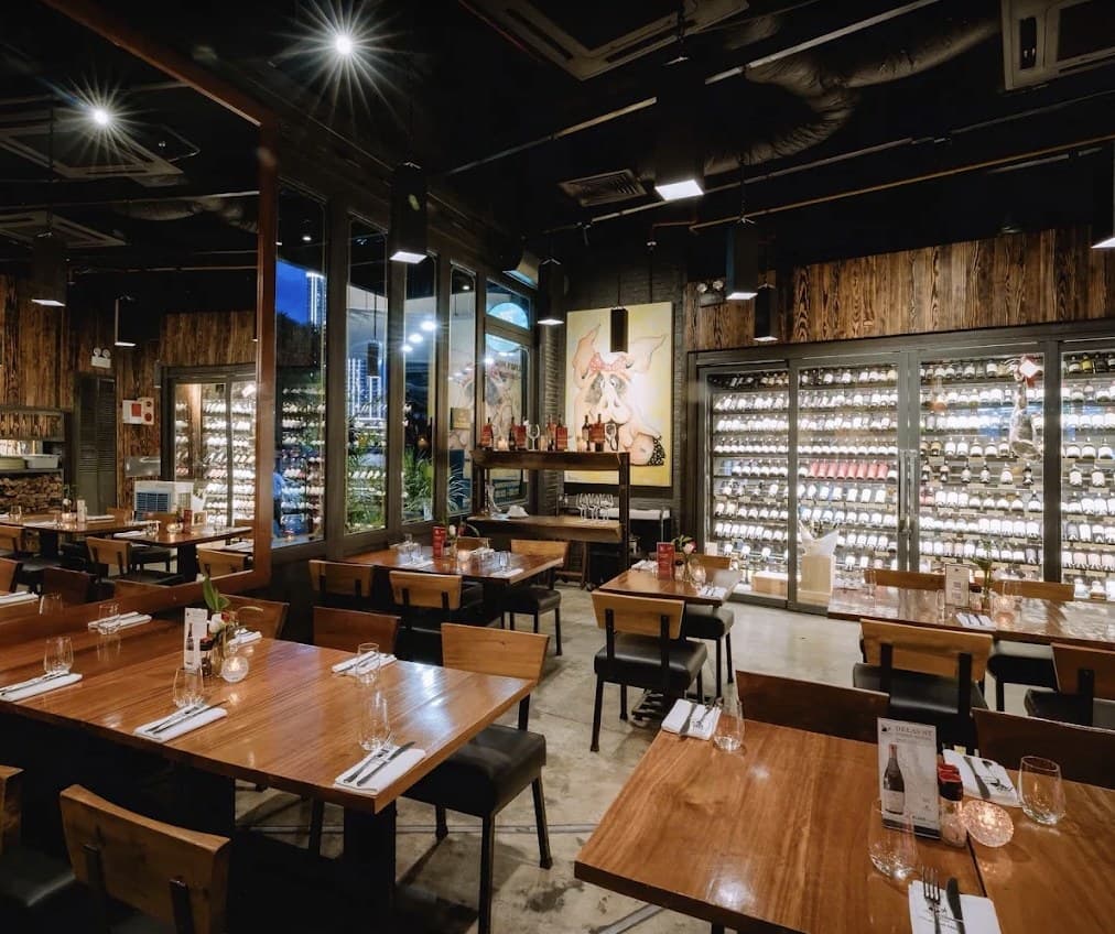 The dining room at Olivia's Prime Steakhouse: wooden tables, a wall of wine bottles behind glass doors, and a painting of a pig with a red bow