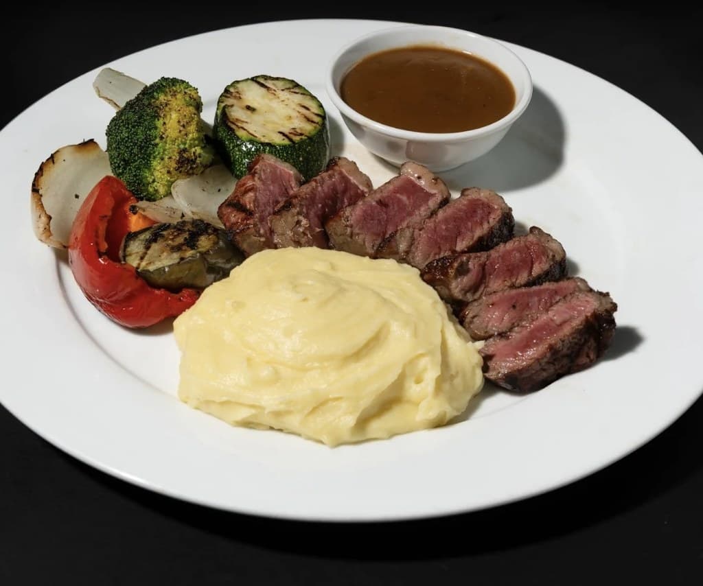A sliced steak at Olivia's Prime Steakhouse with mashed potatoes, grilled vegetables and a small bowl of sauce