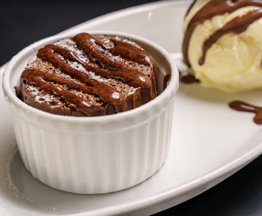 A chocolate cake in a white ramekin at Olivia's Prime Steakhouse, with a scoop of vanilla ice cream and chocolate sauce