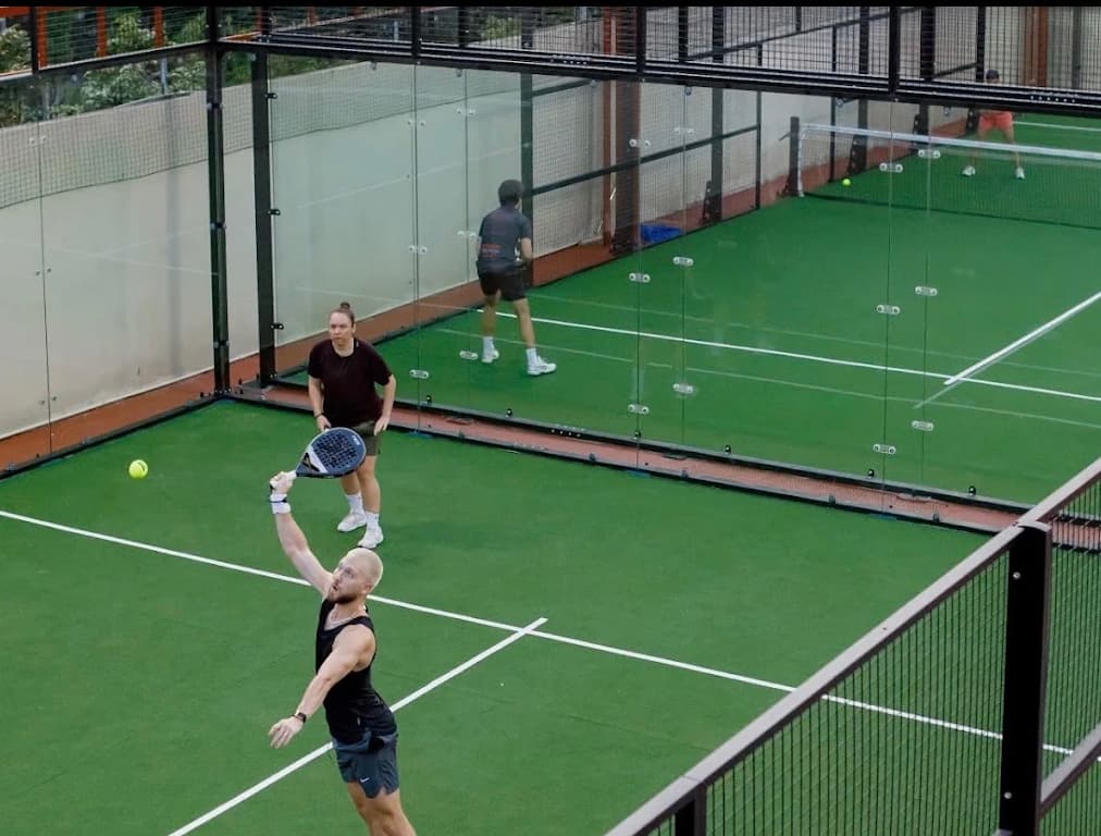 Four players mid rally inside the glass walled padel court at Padel Xtra in Da Nang