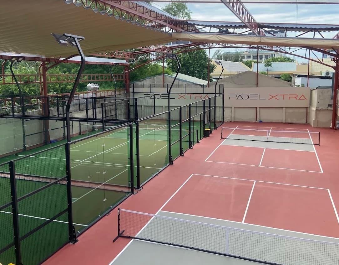 The green glass walled padel court next to the terracotta pickleball court under a canopy at Padel Xtra
