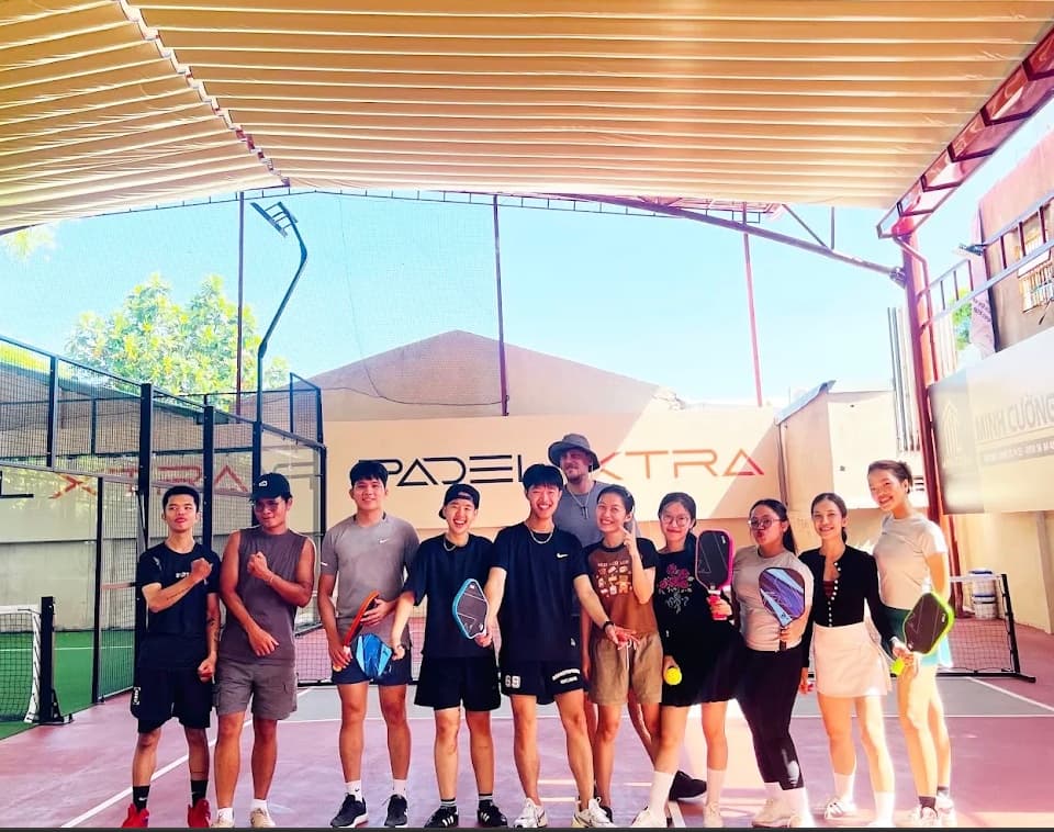 Eleven players standing together holding paddles at Padel Xtra in Da Nang, in front of the padel and pickleball courts