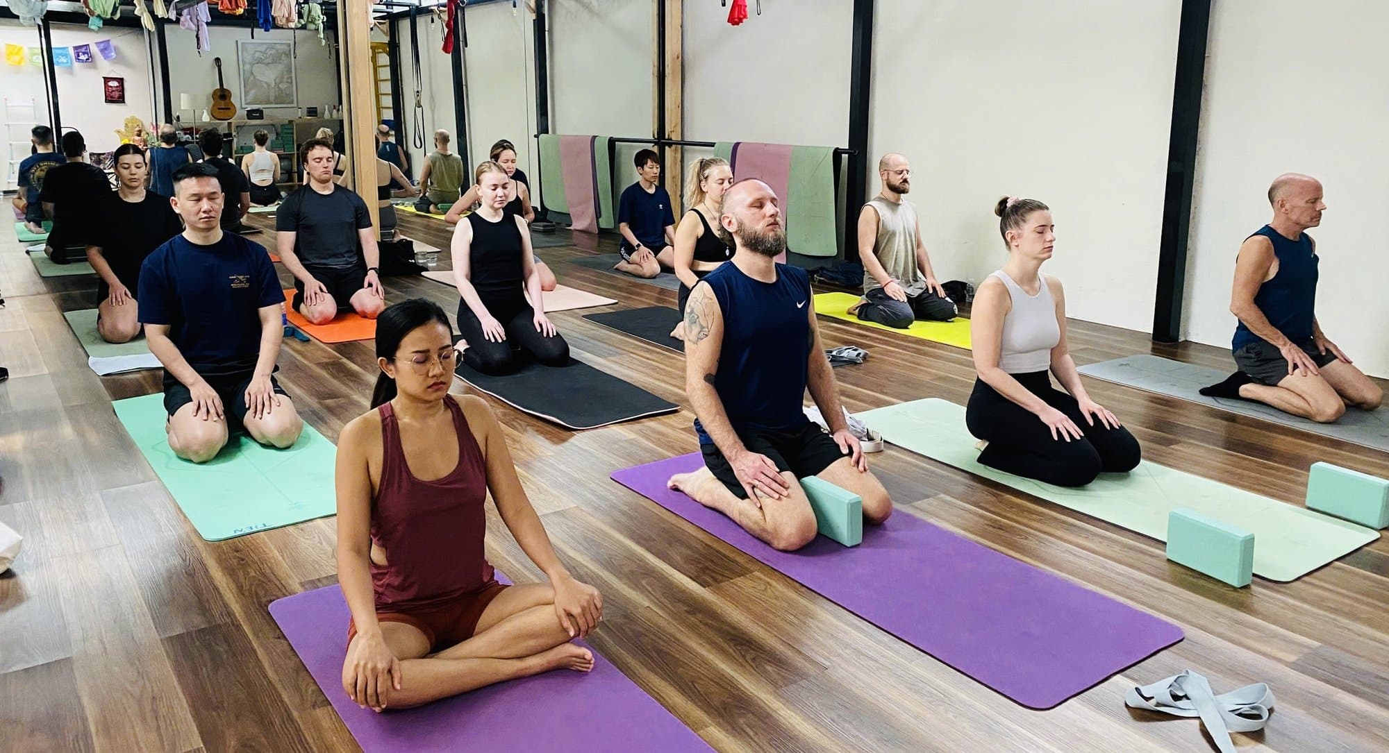Lớp yoga tại Spanda Yoga, mọi người quỳ trên thảm trên sàn gỗ, cờ cầu nguyện ở bức tường xa