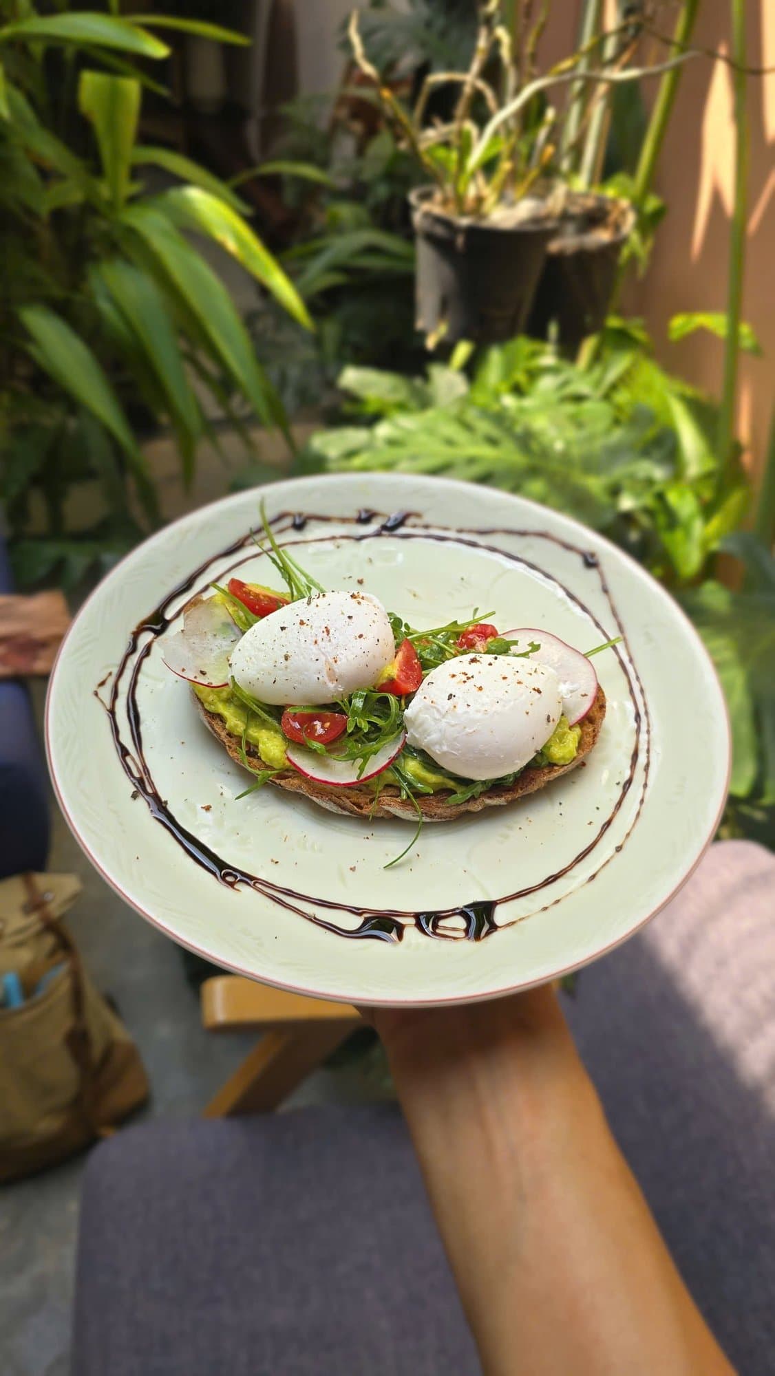 Bánh mì nướng bơ với hai quả trứng chần, cà chua và củ cải đỏ trên đĩa, cầm trên tay trong khu vườn tại Spanda Yoga