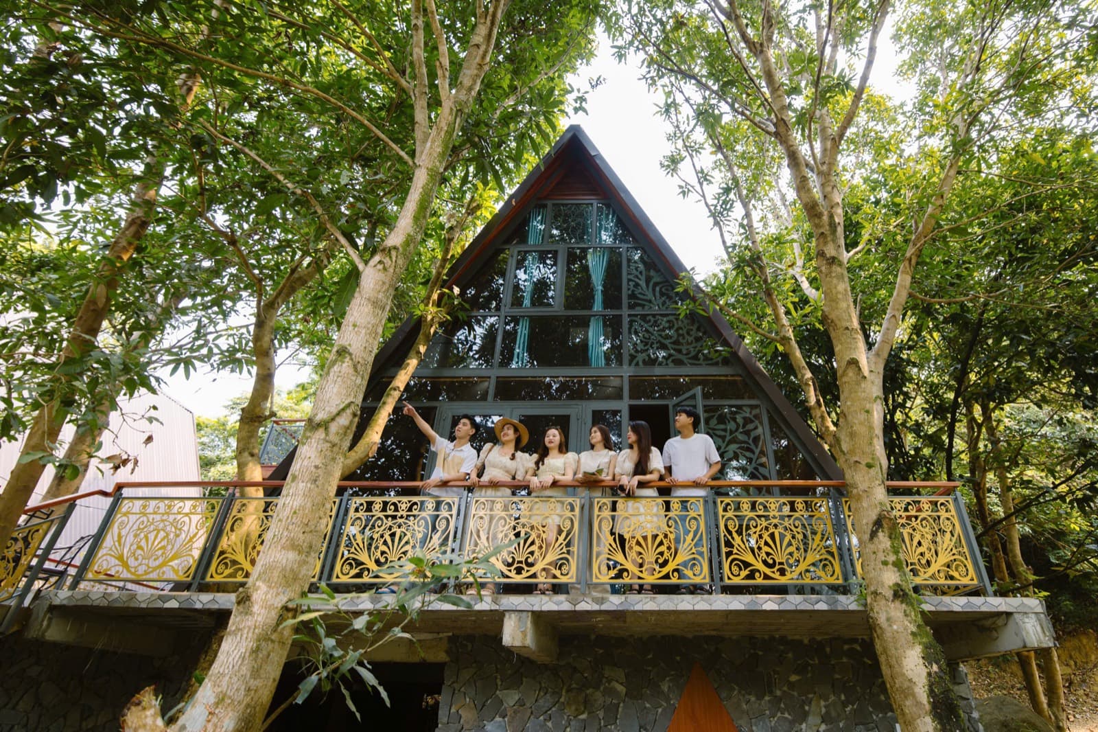 Suối Lương Hải Vân Park, an A-frame villa with a glass front among tall trees, with a group on its balcony