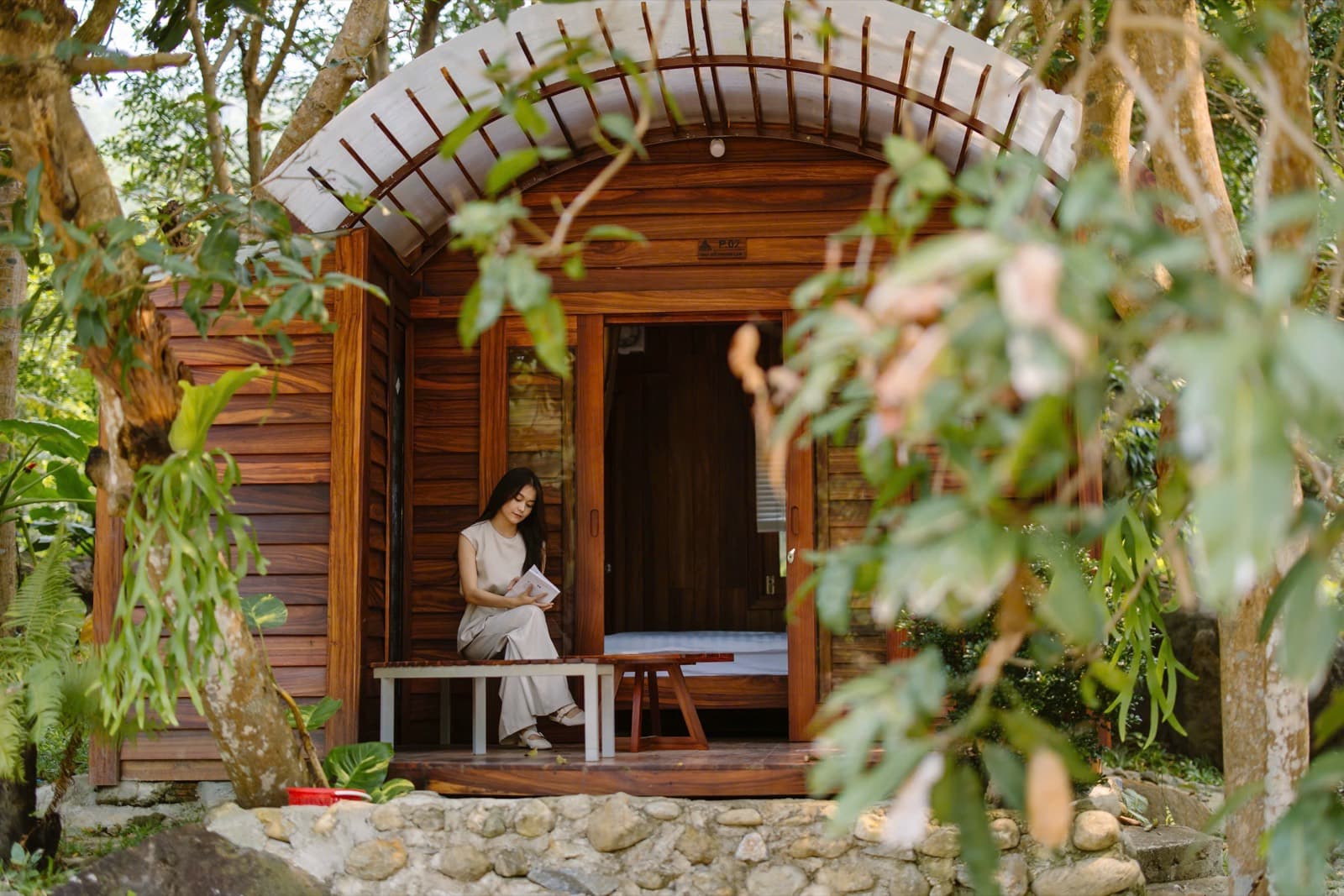 Suối Lương Hải Vân Park, a woman reading on the porch of an arched wooden bungalow among trees