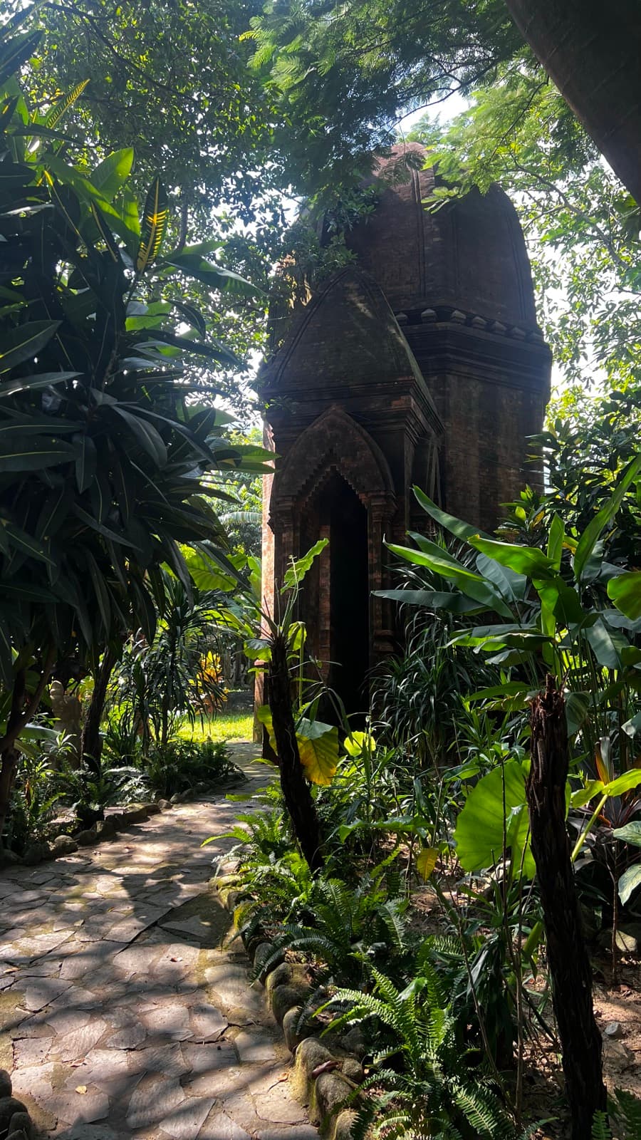 Suối Lương Hải Vân Park, a tall brick tower in the Cham style among tropical plants, beside a stone path