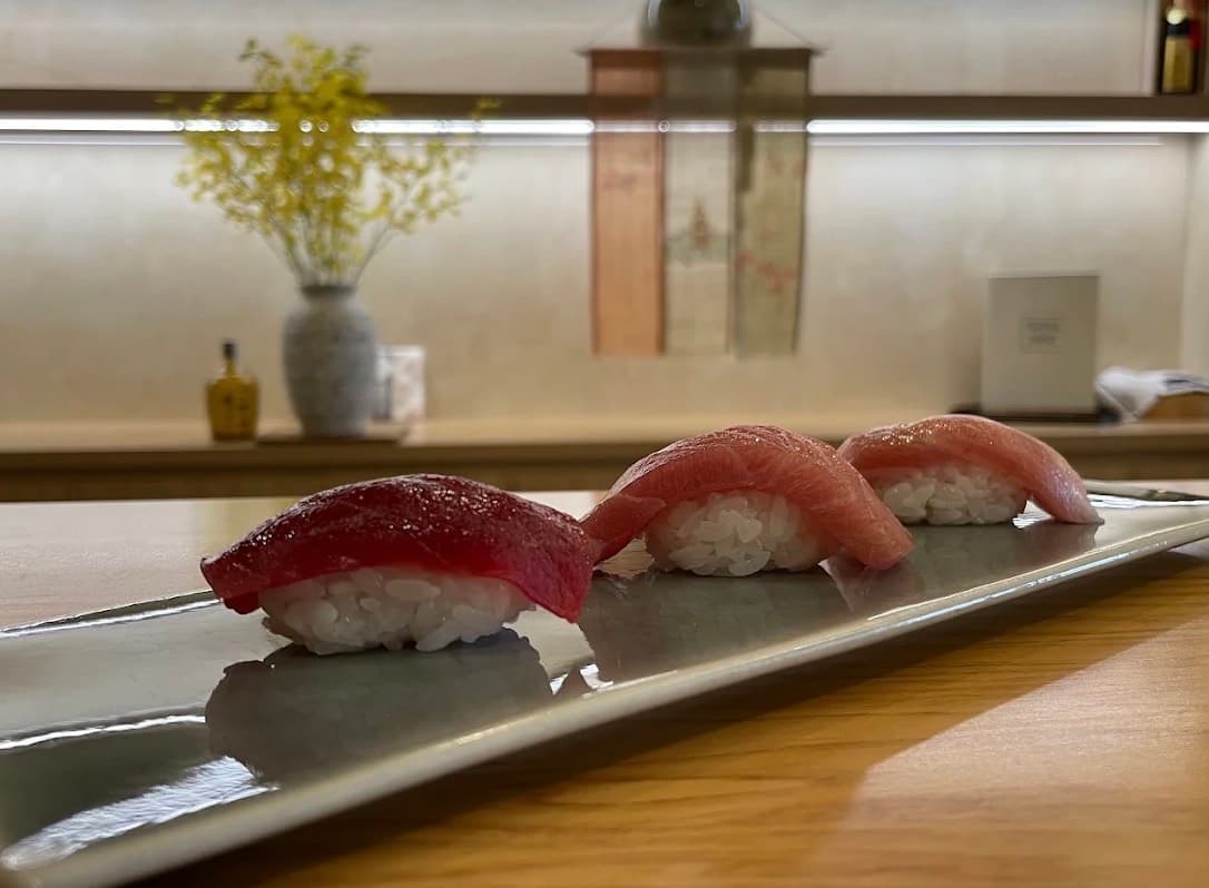 Sushi Seki, ba miếng nigiri cá ngừ xếp thành một hàng trên đĩa dài màu xám, đặt trên quầy gỗ