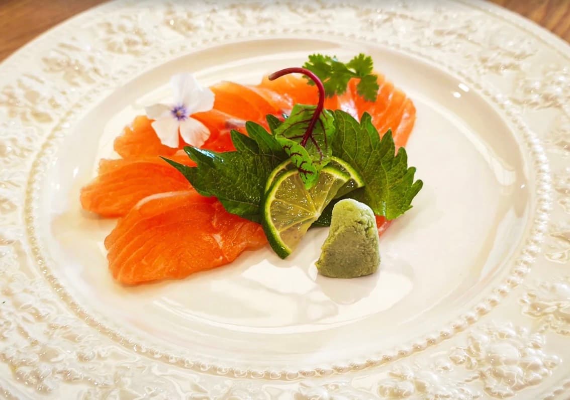 Sushi Seki, sashimi cá hồi với chanh, wasabi, lá tía tô Nhật và một bông hoa trắng trên đĩa trắng