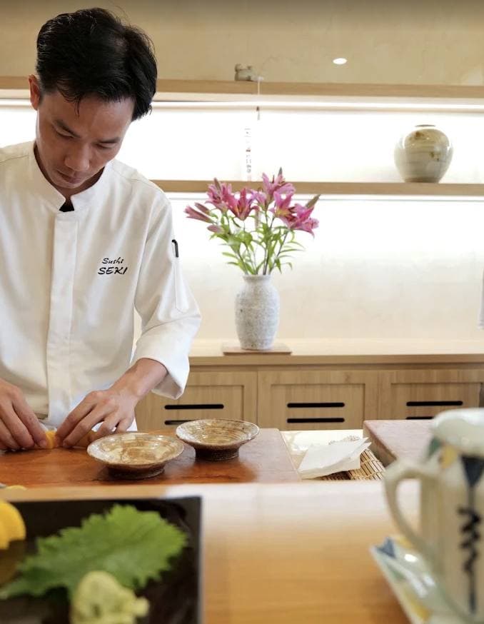 Sushi Seki, đầu bếp mặc áo trắng có chữ Sushi SEKI đang làm sushi tại quầy gỗ