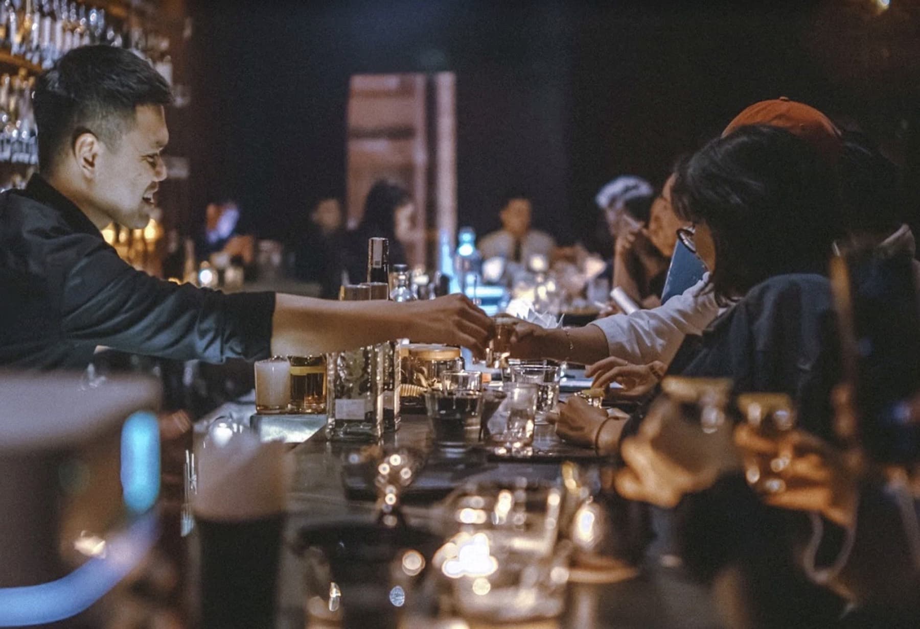 A bartender passing a drink across the bar at Tê Cocktail Bar