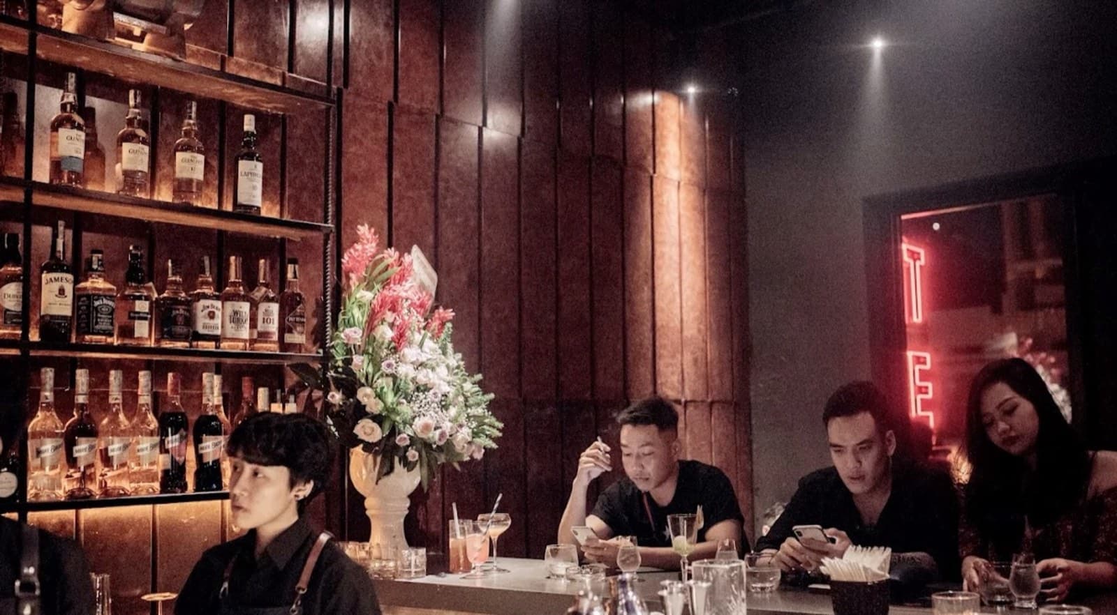 The dark room and neon sign inside Tê Cocktail Bar