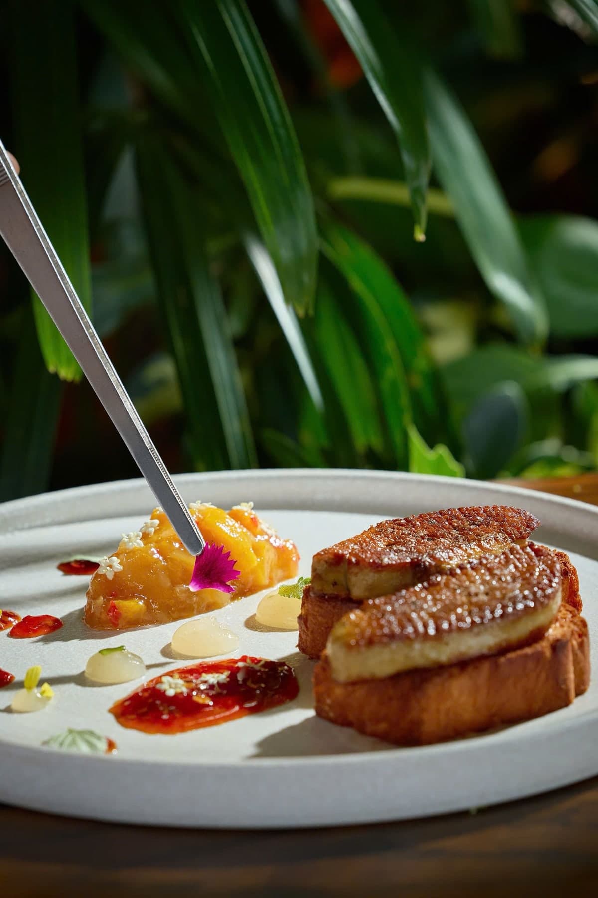 Pan-seared foie gras on toasted brioche at The Gypsy Rooftop Restaurant & Bar, with mango chutney and chili jam, a flower placed with tweezers