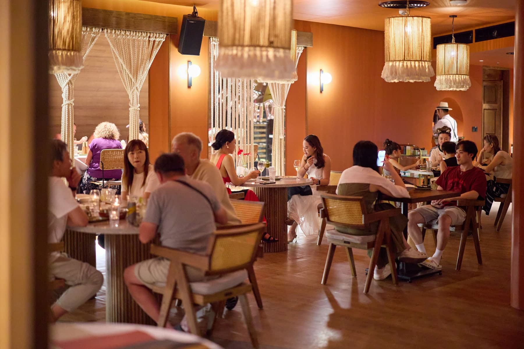 The indoor dining room at The Gypsy Rooftop Restaurant & Bar, with rope lamps, rope curtains and guests at round tables