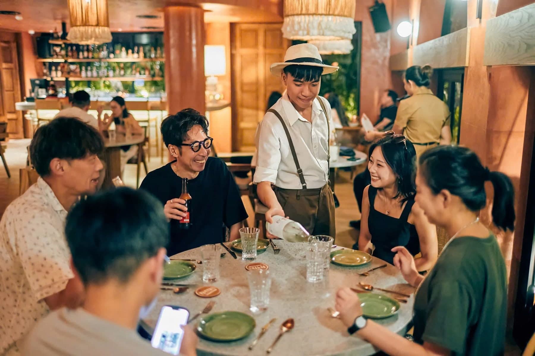 A waiter in a hat pours white wine for a table of five at The Gypsy Rooftop Restaurant & Bar