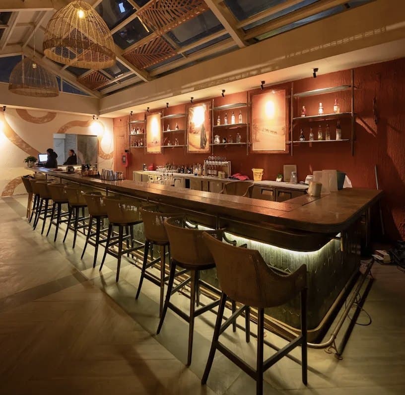 Quầy bar của The Roof: quầy dài với hàng ghế cao, tường màu đỏ và kệ chai có đèn