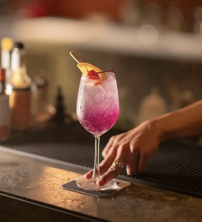 Một ly cocktail màu hồng trong ly rượu vang trên quầy bar ở The Roof