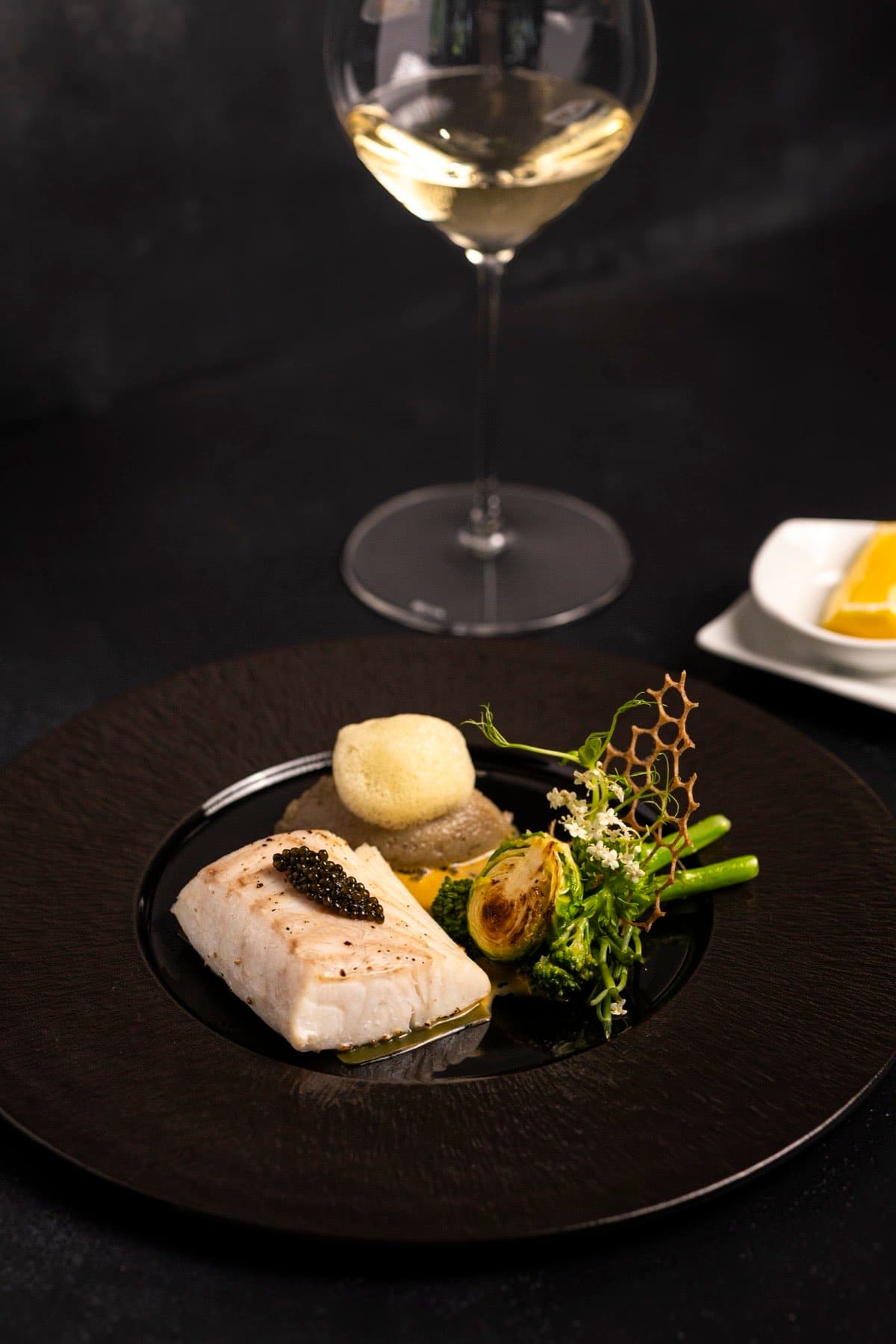 The Temptation, một miếng cá trắng phủ trứng cá caviar, bên cạnh ly rượu vang trắng
