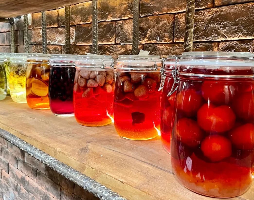 A shelf of glass jars behind the bar at United Bar, holding strawberries, plums and berries infusing in spirit